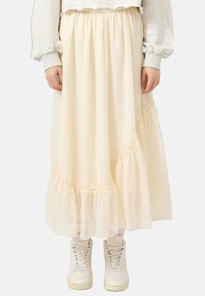 Langer Rock in Cremefarbe mit gerafftem Volantdetail, getragen mit hellgrauem Sweatshirt und weißen High-Top-Sneakern.