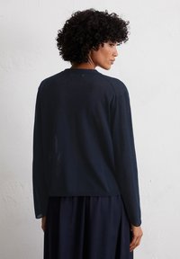 Haut à manches longues bleu marine foncé avec une coupe décontractée, un col rond et une texture douce. Le tissu semble léger avec des coutures minimales.