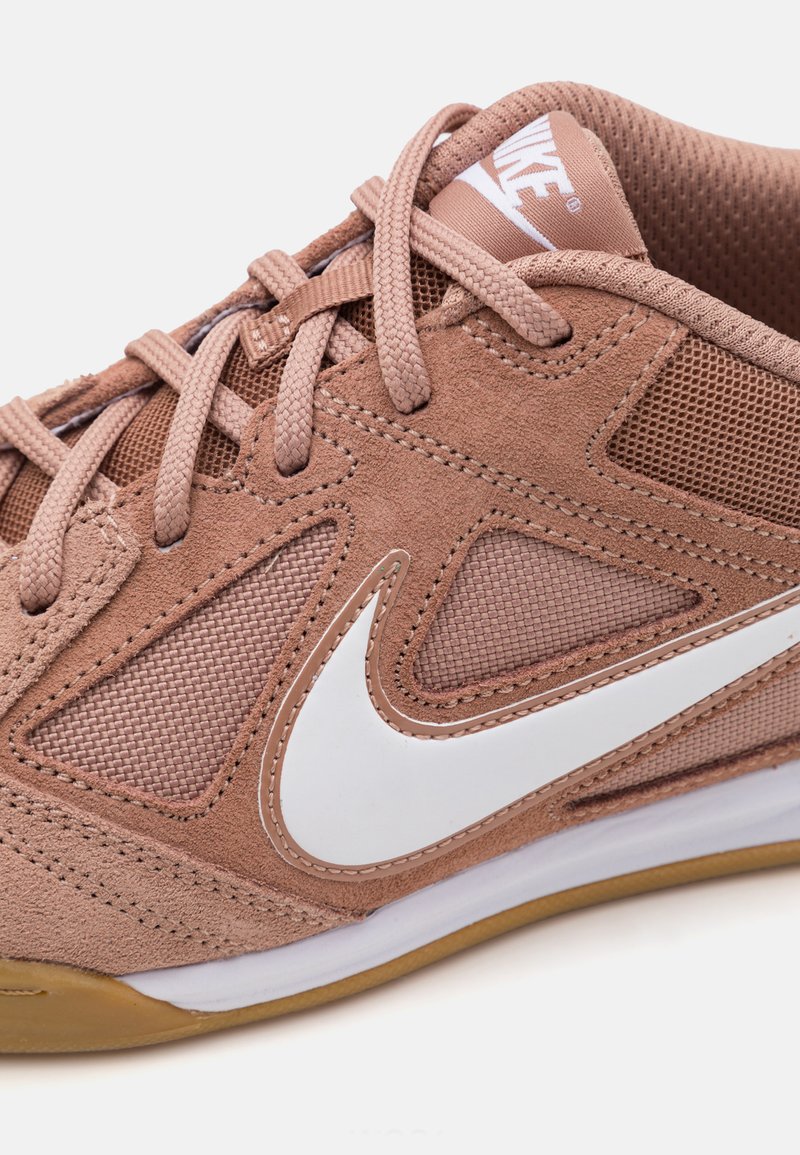 Zapatillas Nike en ante y malla de color marrón claro, con un swoosh blanco, cordones redondos y una suela de goma con una superficie texturizada.