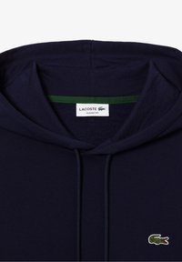 Mörkblå hoodie i bomull med en grön innerkrage, framsnoddar och en liten broderad krokodillogo på bröstet.