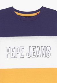 Tričko s proužky v námořnické modři, bílé a hořčicové, vyrobené z bavlny. Má kulatý výstřih a uprostřed výrazně vytištěný nápis "PEPE JEANS".