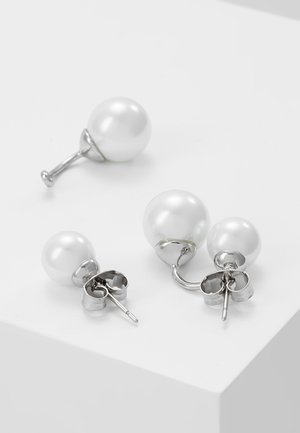 Boucles d’oreilles clous en argent avec des perles blanches rondes, une paire avec double perles et une boucle d’oreille simple en perle placées sur une surface blanche.