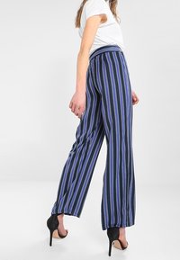 Pantalones de pierna ancha en navy con rayas verticales en púrpura y blanco. Presentan una cintura alta y una tela ligera. Se combinan con tacones negros.