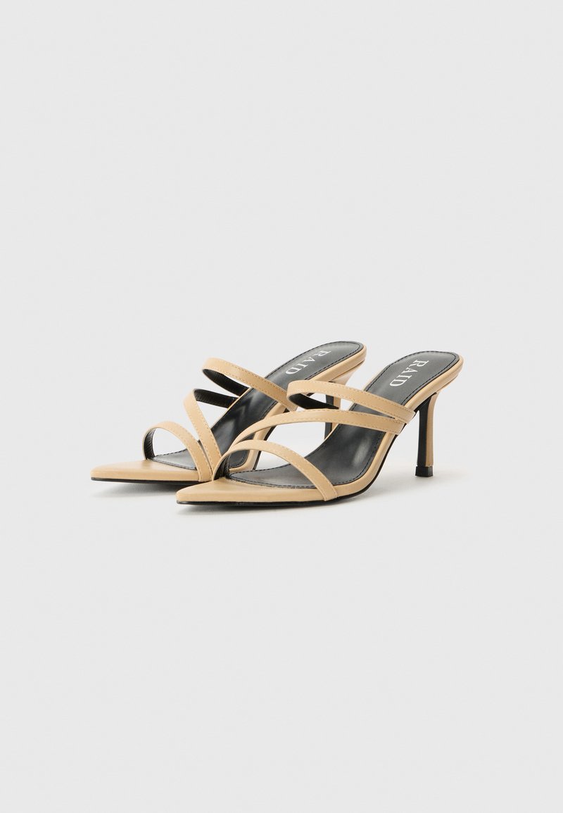 Sandales à talons hauts taupe avec des sangles croisées, design à bout ouvert et un talon fin. Semelle intérieure noire avec le logo de la marque en haut. Texture lisse.