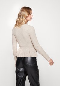 Maglione beige a coste con maniche lunghe e orlo a peplo, abbinato a pantaloni in pelle nera. La morbida texture e il design aderente esaltano la silhouette.