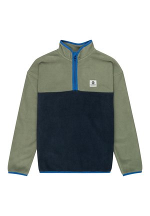 Enfant portant un pull polaire vert et bleu marine, un pantalon cargo vert olive, et des baskets bleu marine avec des semelles en gomme, debout devant un fond uni.