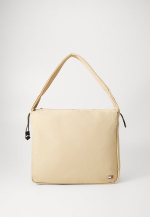 Bolsa de ombro em náilon bege com uma textura suave, um corpo largo, uma alça ajustável e fecho com zíper. Inclui uma etiqueta de logotipo na frente.