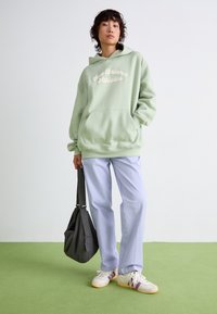 Mintgrön hoodie med frontficka och vit text "New Balance Athletics", ihop med ljuslila byxor och vita sneakers med lila detaljer.