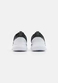 Chaussures de sport noir et blanc avec une tige en maille, semelle blanche rembourrée et languettes au talon pour un enfilage facile.