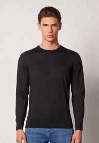 Svart långärmad tröja med enkel rund halsringning, tillverkad av ett mjukt material, med ribbade ärmslut och nederkant. Bärs över blå jeans.