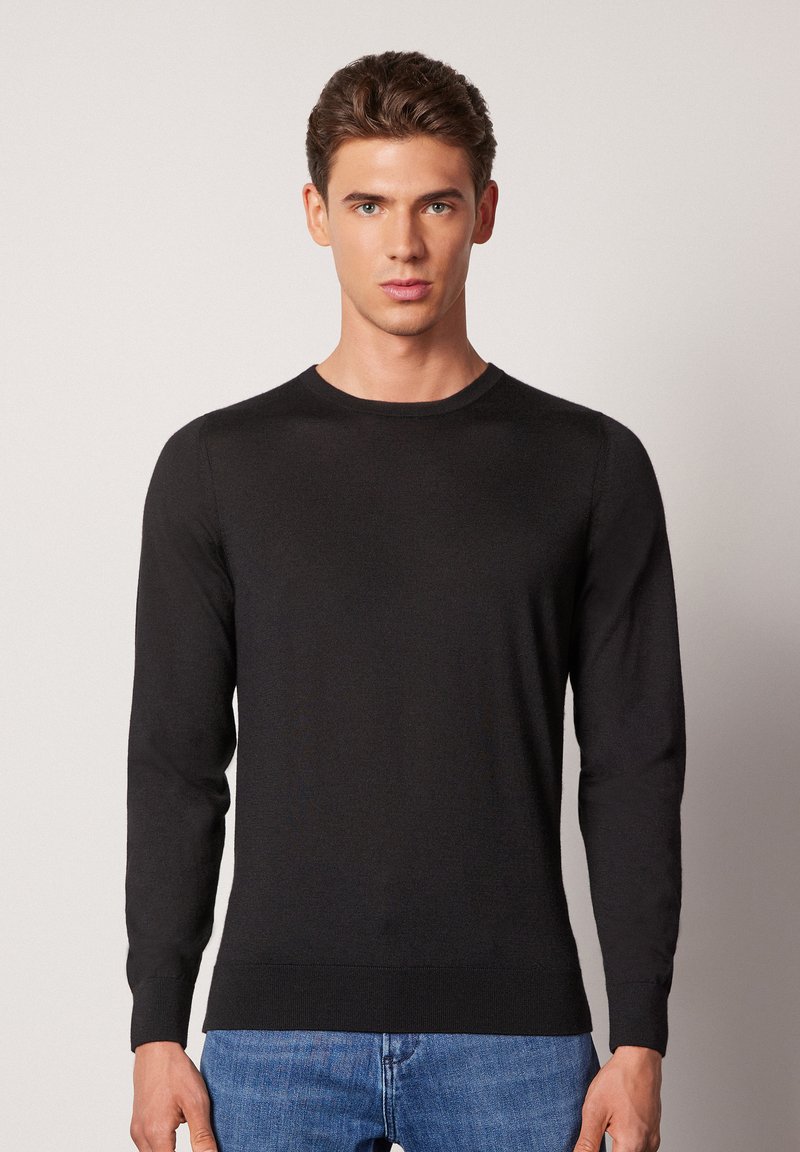 Svart långärmad tröja med enkel rund halsringning, tillverkad av ett mjukt material, med ribbade ärmslut och nederkant. Bärs över blå jeans.