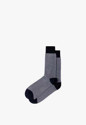 Par de calcetines hasta media pantorrilla con pequeño patrón de rombos en negro y blanco, puños, talones y dedos negros sobre fondo blanco.