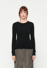 Haut noir à manches longues en rib, avec un col rond et une silhouette ajustée, associé à un pantalon large texturé gris.