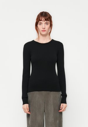 Svart ribbestrikket topp med lange ermer og rund hals, kombinert med teksturerte grå vide bukser.
