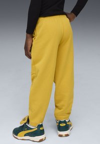 Gule bomulds sweatpants med løs pasform, elastisk talje, sidelommer, parret med grønne og hvide sneakers med et logo.