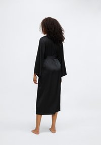 Μαύρη μακριά ρόμπα με λεία υφή, μακριά μανίκια και ζώνη στη μέση. Διαθέτει πλαϊνές σχισμές και ίσια γραμμή, φτάνει μέχρι το μέσο της κνήμης.