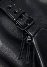 Black leather bag featuring a textured surface, prominent silver hardware, a strap with circular cutouts, and dual zipper pulls for closure.