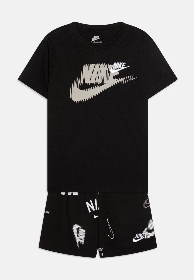 Fekete pamut póló fehér Nike logóval, fekete rövidnadrággal párosítva, amelyeken szétszórtan találhatók fehér Nike márkajelzés és logók.