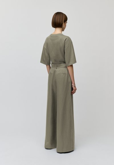 Khakifarbenes, weit geschnittenes Jumpsuit mit lockerem Sitz, kurzen Ärmeln und einem Taillengürtel. Die Rückseite verfügt über zwei aufgesetzte Taschen und hat eine glatte Textur.