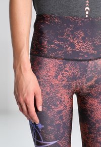 High-waist leggings in zwart en rood met een gespikkeld patroon. Gemaakt van een rekbare stof, voorzien van een gladde tailleband en minimale naden.