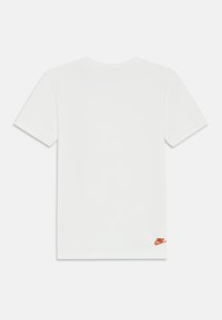 T-shirt bianco a maniche corte in cotone, con un piccolo logo Nike arancione in basso a sinistra. Tessuto morbido, vestibilità classica.