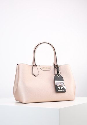 Sac à main en cuir rose clair avec des doubles anses et une étiquette noire Karl Lagerfeld avec un motif de dessin animé portant des lunettes de soleil.