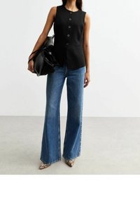 Černý bezrukávový top s předními knoflíky, v kombinaci s modrými širokými džínami. Mezi výrazné detaily patří strukturovaný silueta a texturovaná tkanina.