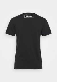 Černé bavlněné tričko s krátkým rukávem, kulatým výstřihem a bílým vyšívaným logem "guess" na zadní straně. Jednoduchá barva, elegantní design.