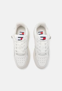 Białe sneakersy z perforowanym wzorem na czubku, górna część z gładkiej skóry, sznurowadła i metka z logo w kolorach niebieskim i czerwonym na języku.