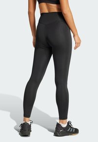 Sorte højtaljede leggings lavet af strækbart stof, med en glat tekstur og flade sømme. Sammen med sorte træningssko.