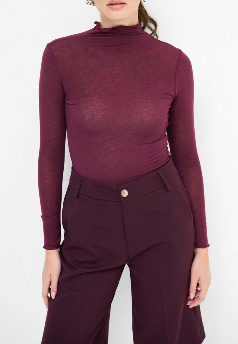 Maglia a maniche lunghe bordeaux con collo alla coreana, dal design aderente, abbinata a pantaloni bordeaux a vita alta con dettaglio centrale a bottoni.