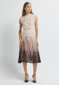 Vestido de seda sin mangas con estampado de tie-dye en beige y marrón oscuro. Presenta una cintura ajustada y una falda fluida con pliegues que cae a mitad de la pantorrilla.