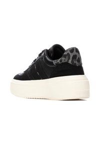 Zapatillas negras de plataforma con parte superior texturizada, que cuentan con un acento de talón de piel de leopardo y una gruesa suela de goma blanca.