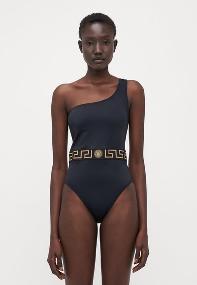 Maillot de bain une pièce noir avec une seule bretelle, une ceinture accentuée en or au motif grec, et un matériau lisse et ajusté.