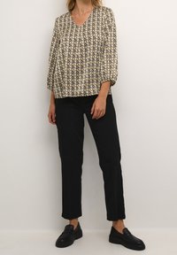 Blusa de estampado floral en tonos crema, negro y mostaza; mangas abullonadas; escote en V; combinada con pantalones negros de corte tailoring y mocasines negros.