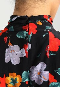 Schwarzer Stoff mit floralem Muster in Rot, Orange und Lila; Design mit hohem Kragen; Reißverschlussdetail im Rücken; glatte, leichte Textur.