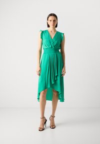 Green, knee-length dress with a deep V-neck, ruffled sleeves, and an elastic smocked waist. Features an asymmetrical hemline and flowing fabric.