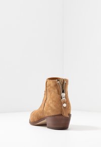 Kotníková bota z broušené kůže v barvě světle hnědé s bočním zipem, zaoblenou špičkou a nízkým dřevěným blokovým podpatkem. Hladká textura s minimálním zdobením.