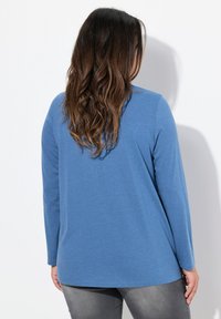 Blaues Langarmoberteil mit lockerer Passform, aus weichem Material gefertigt. Verfügt über einen runden Ausschnitt und eine schlichte Textur, kombiniert mit grauen Jeans.