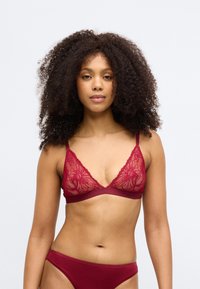 Čipkasti crveni bralet sa trokutastim oblikom, cvjetnim uzorkom i podesivim naramenicama. Uparen sa crvenim gaćicama koje imaju glatku teksturu.