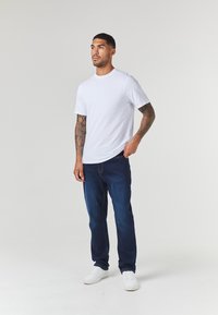 Camiseta blanca de manga corta combinada con jeans azul oscuro y zapatillas blancas. Los jeans tienen bolsillos estándar y un diseño de pierna recta.