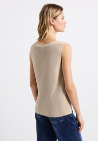 Top senza maniche beige con texture a costine, con scollatura rotonda. Indossato con jeans in denim blu, che accentuano un fit rilassato.