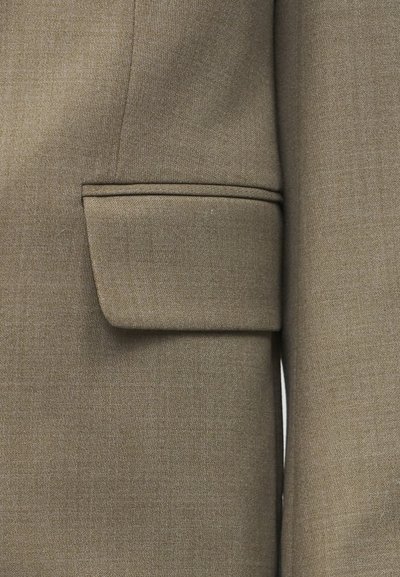 Προσαρμοσμένο χακί σακάκι με τσέπη με καπάκι και ορατές λεπτομέρειες ραφής σε υφή υφάσματος.