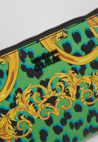 Pochette verte avec imprimé léopard noir et bleu, volutes baroques jaunes ornées, fermeture éclair noire et logo noir « Versace Jeans Couture ».