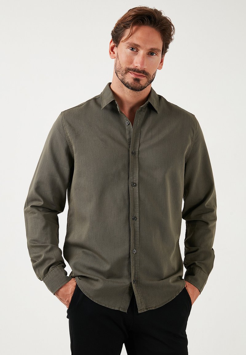 Camisa de manga larga de color verde oliva en tejido texturizado, con cuello abotonado, que presenta un cierre frontal de botones y un diseño ajustado.