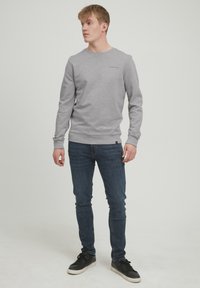 Grauer Sweatshirt mit Rundhalsausschnitt, gerippten Bündchen und Saum. Getragen mit dunkelblauen Slim-Fit-Jeans und schwarzen Sneakers. Minimalistisches Design, keine Muster.
