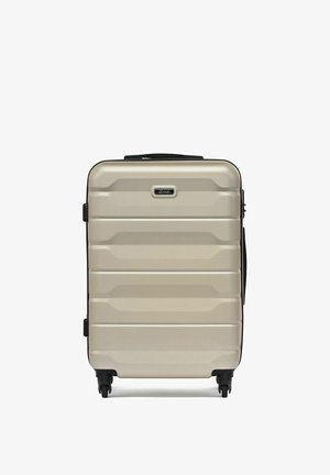 Beżowa walizka z twardą powłoką, posiadająca cztery czarne kółka, górny uchwyt oraz poziome rowki na powierzchni.