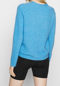 Suéter de lana azul claro con un tejido texturizado, cuello redondo y mangas largas, combinado con pantalones cortos ajustados negros.