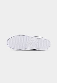 Semelle d'une basket blanche avec un motif de bande de roulement hexagonal et le logo "GAP" embossé au centre sur un fond clair uni.