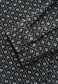 Wool blend fabric in a black and white geometric pattern, featuring a black button on the cuff, with a textured appearance.